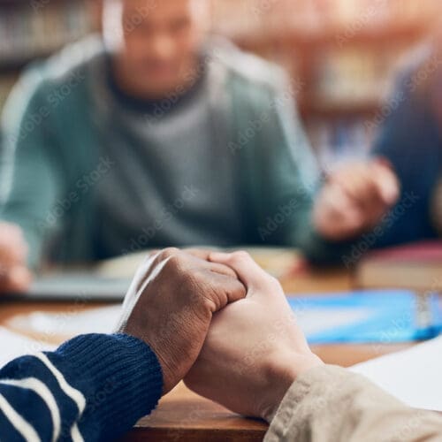 stock image - Students holding hands around a table.