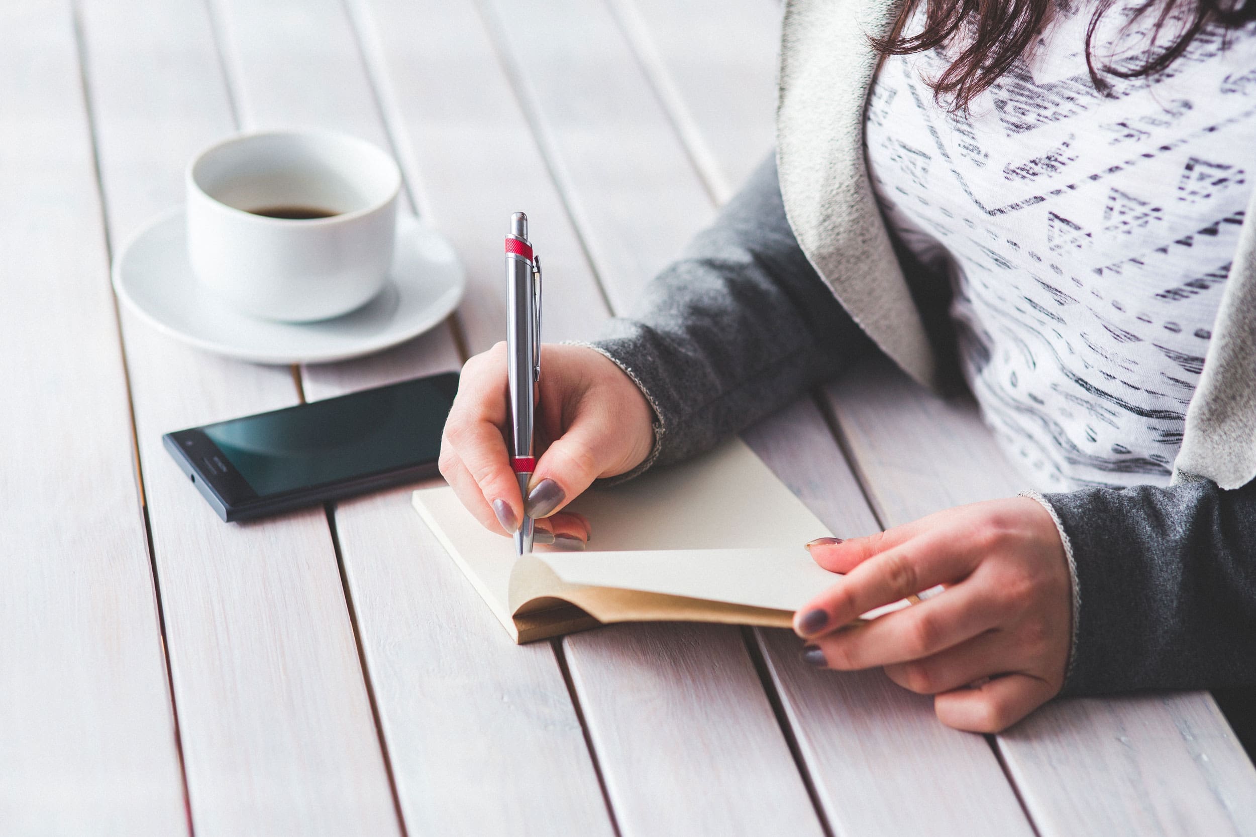a student writing at an outdoor table with a coffee cup and her smartphone