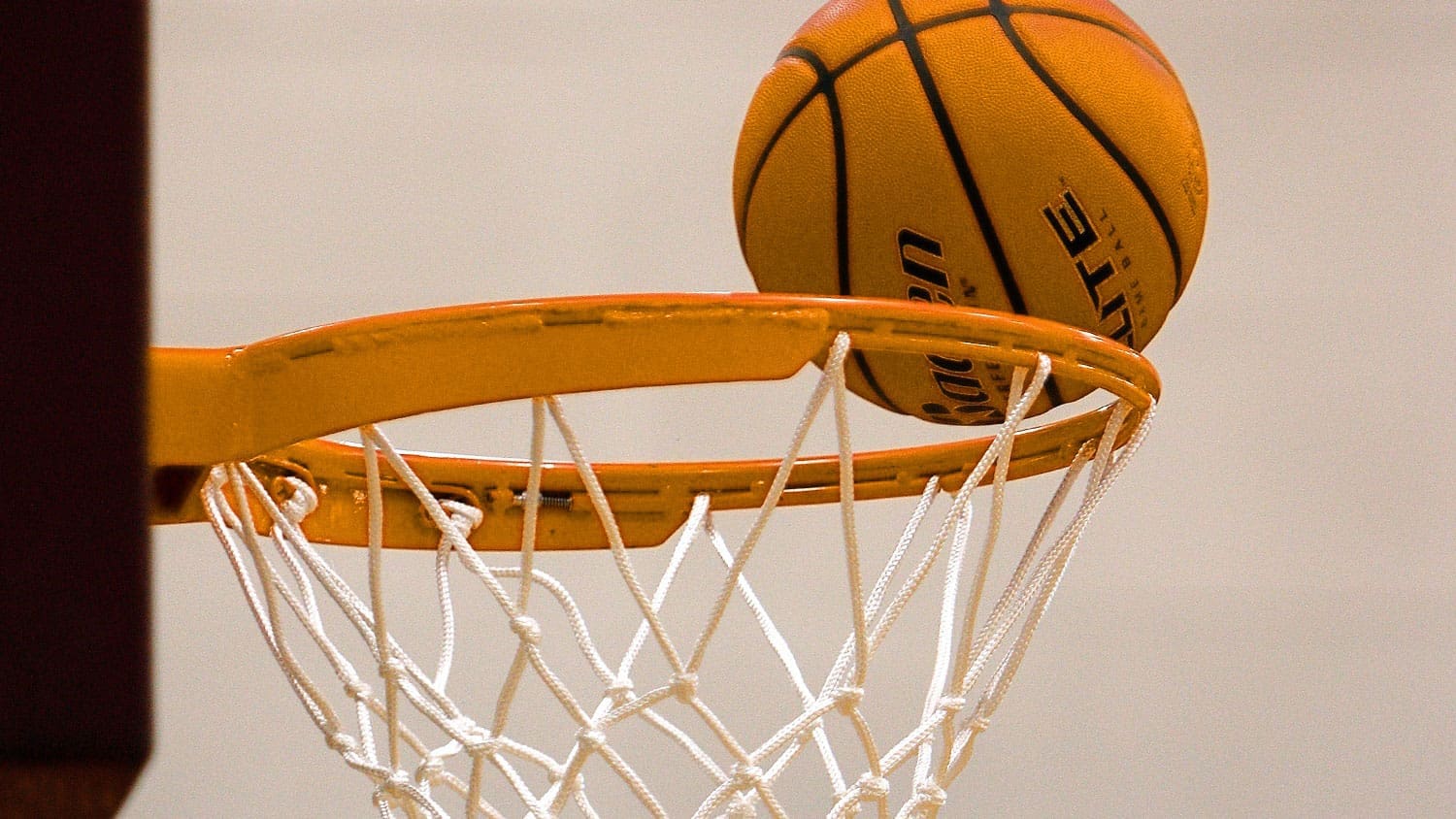 A TLU-gold basketball going in a basket.